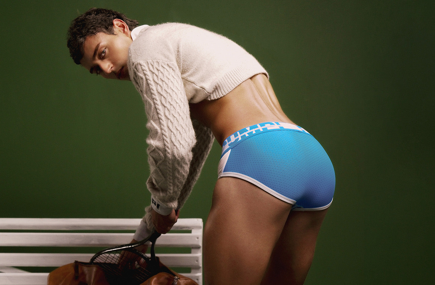 Model in the blue PUMP! Match Point Brief leaning over a courtside bench, rear view